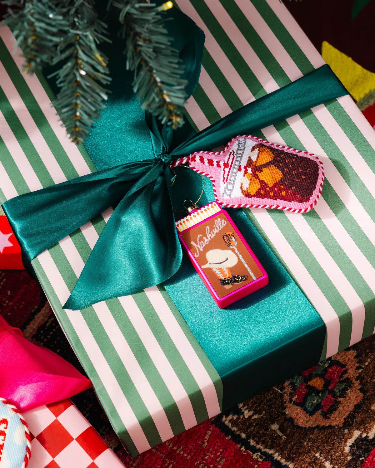 Needlepoint soda bottle ornament resting on a striped gift box with teal ribbon