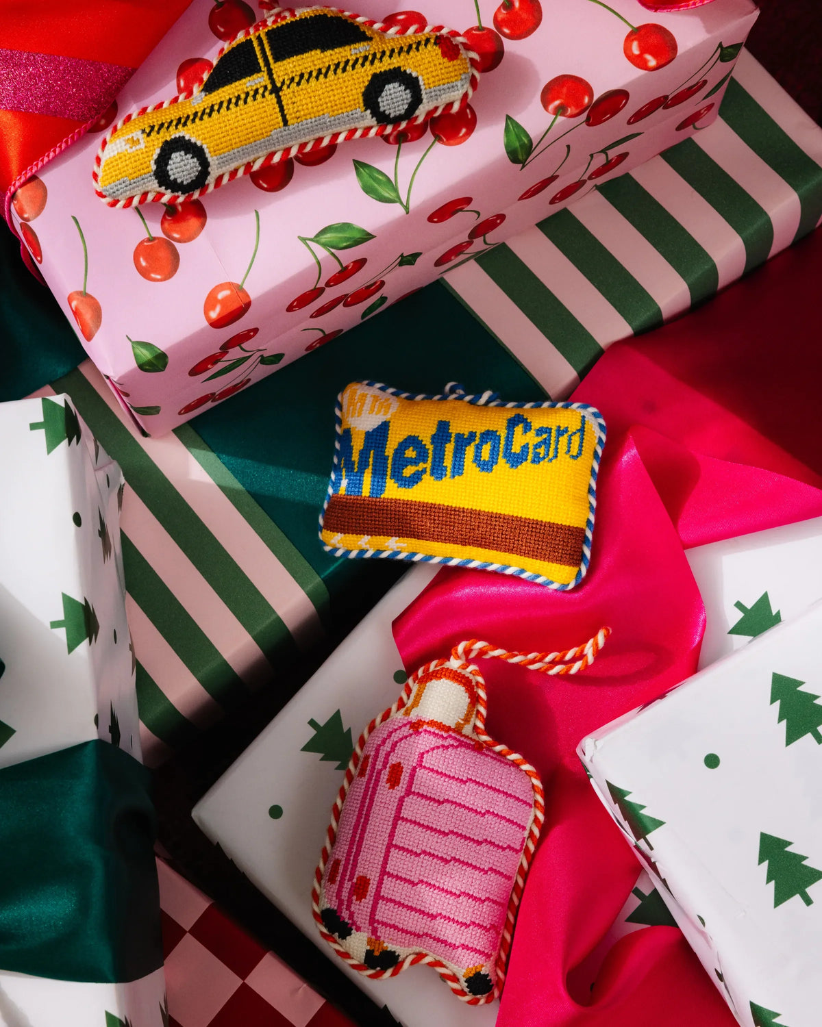 Pink luggage-shaped needlepoint ornament lying among wrapped gifts