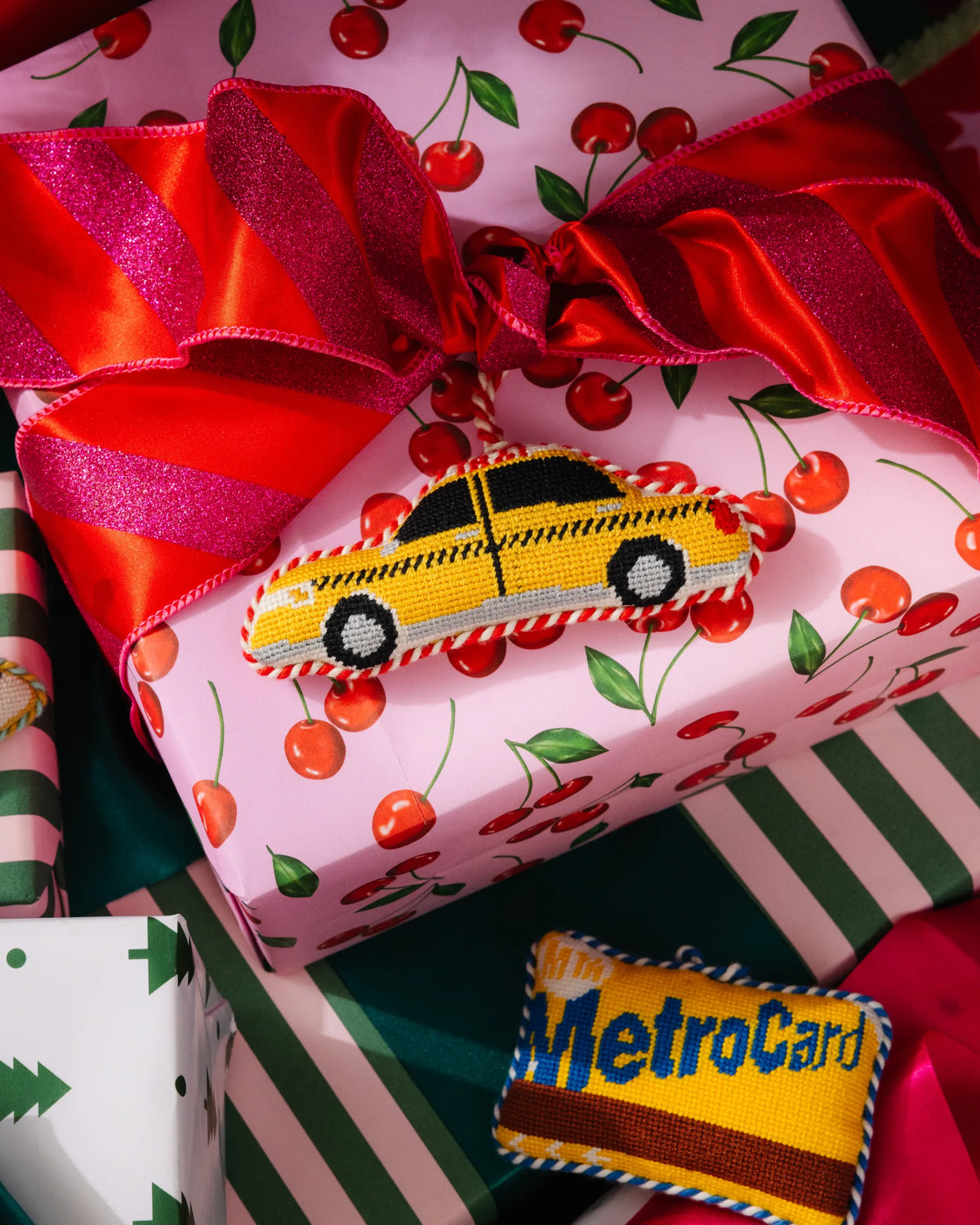 Needlepoint taxi cab ornament on patterned gift wrap with red ribbon