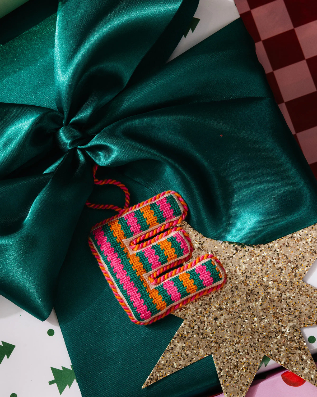 Needlepoint letter E ornament with multicolor stitched rows and braided loop for hanging.