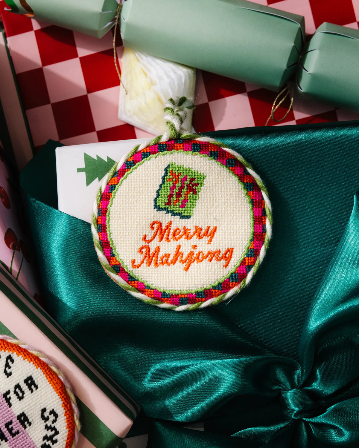 Round needlepoint ornament with braided loop, green mahjong icon, and “Merry Mahjong” text