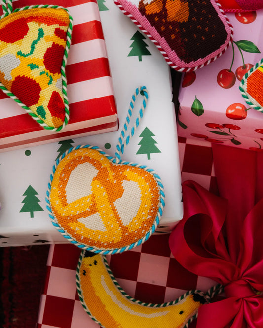 Needlepoint pretzel icon ornament in orange and white cross-stitch with blue hanging loop