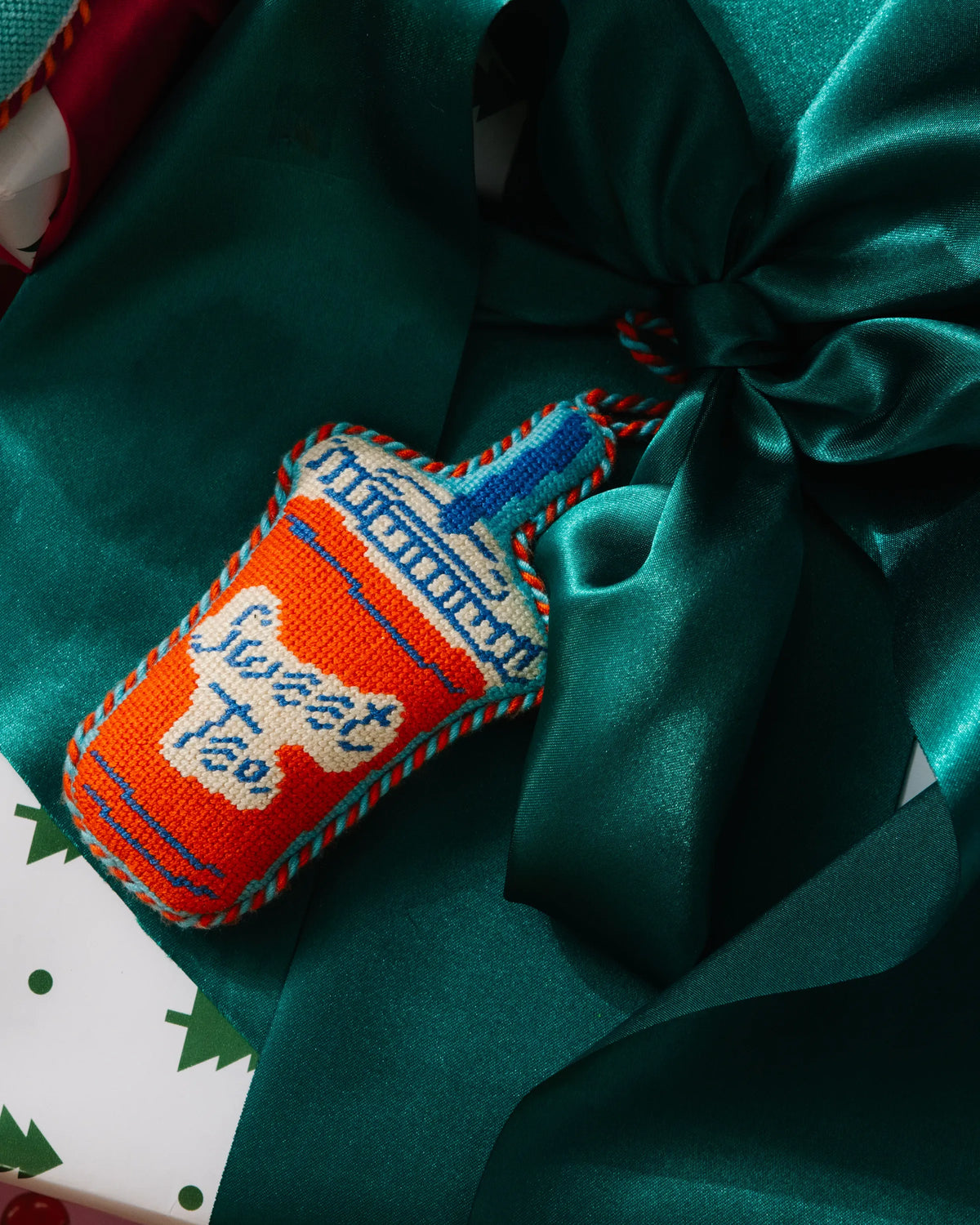 Needlepoint bottle ornament with embroidered script detail beside a teal bow