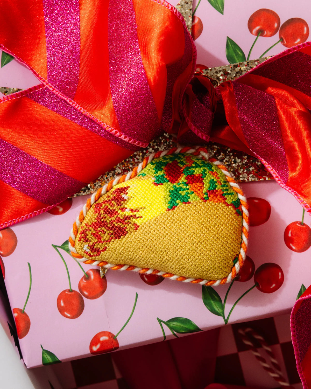 Needlepoint taco ornament under a red ribbon and bow with berries
