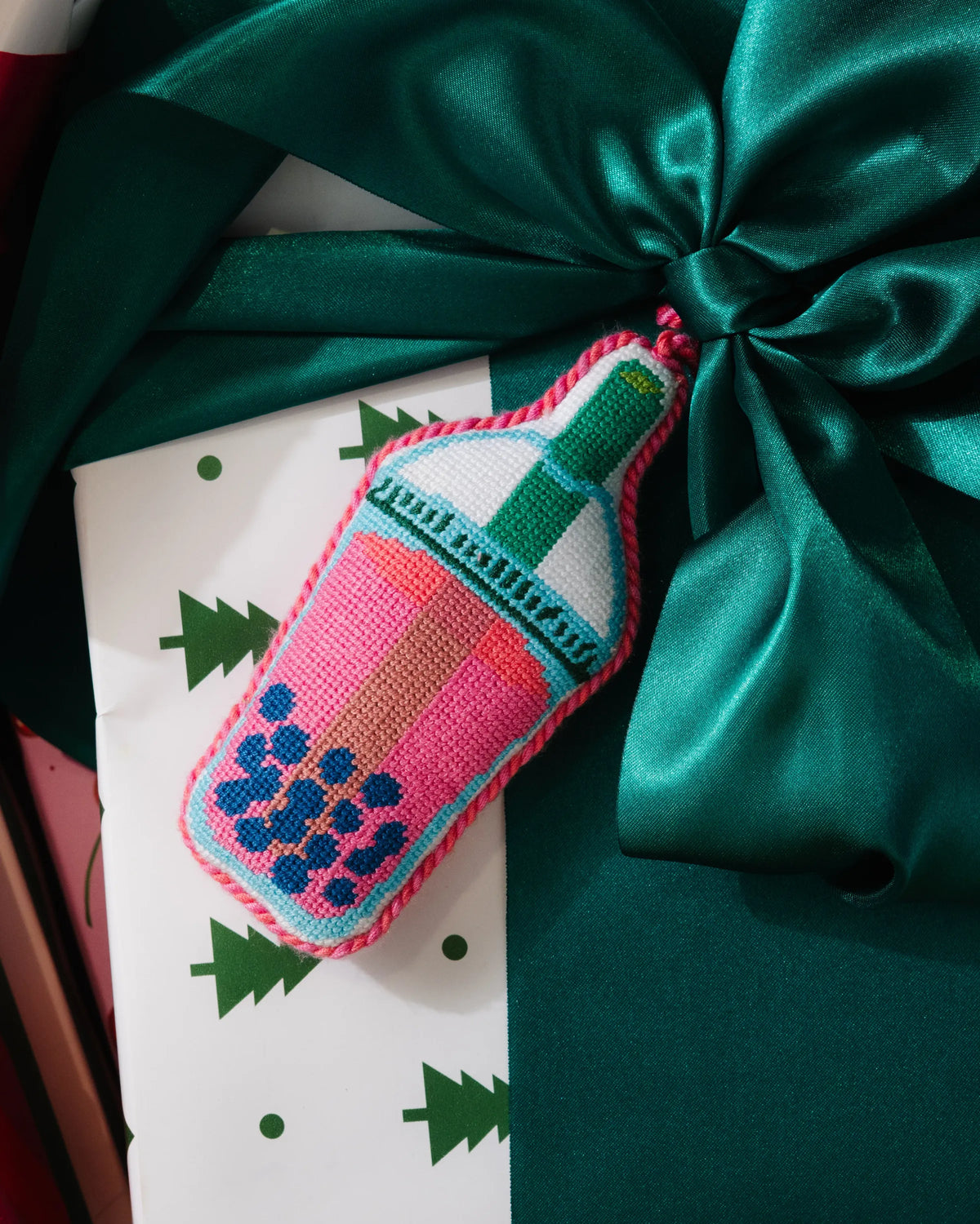 Needlepoint boba icon ornament on gift with teal ribbon bow, stitched bottle hanging