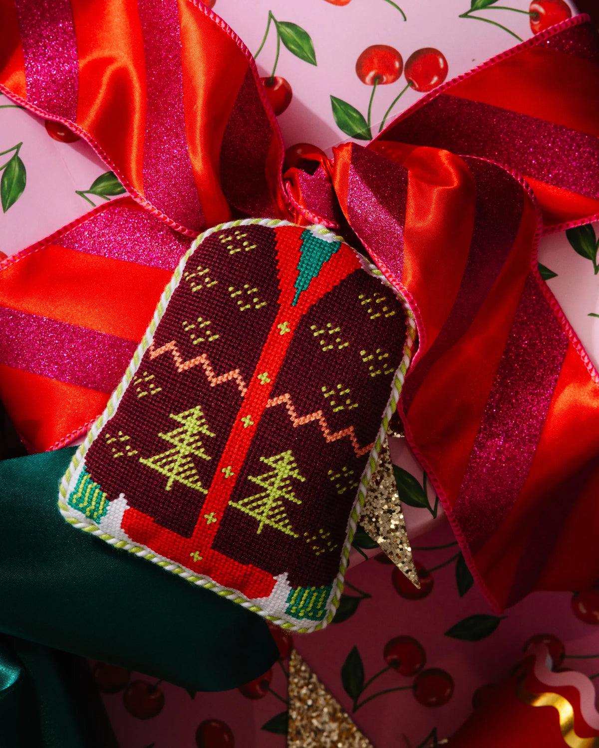 Needlepoint sweater icon ornament with braided hanger tucked under red bow