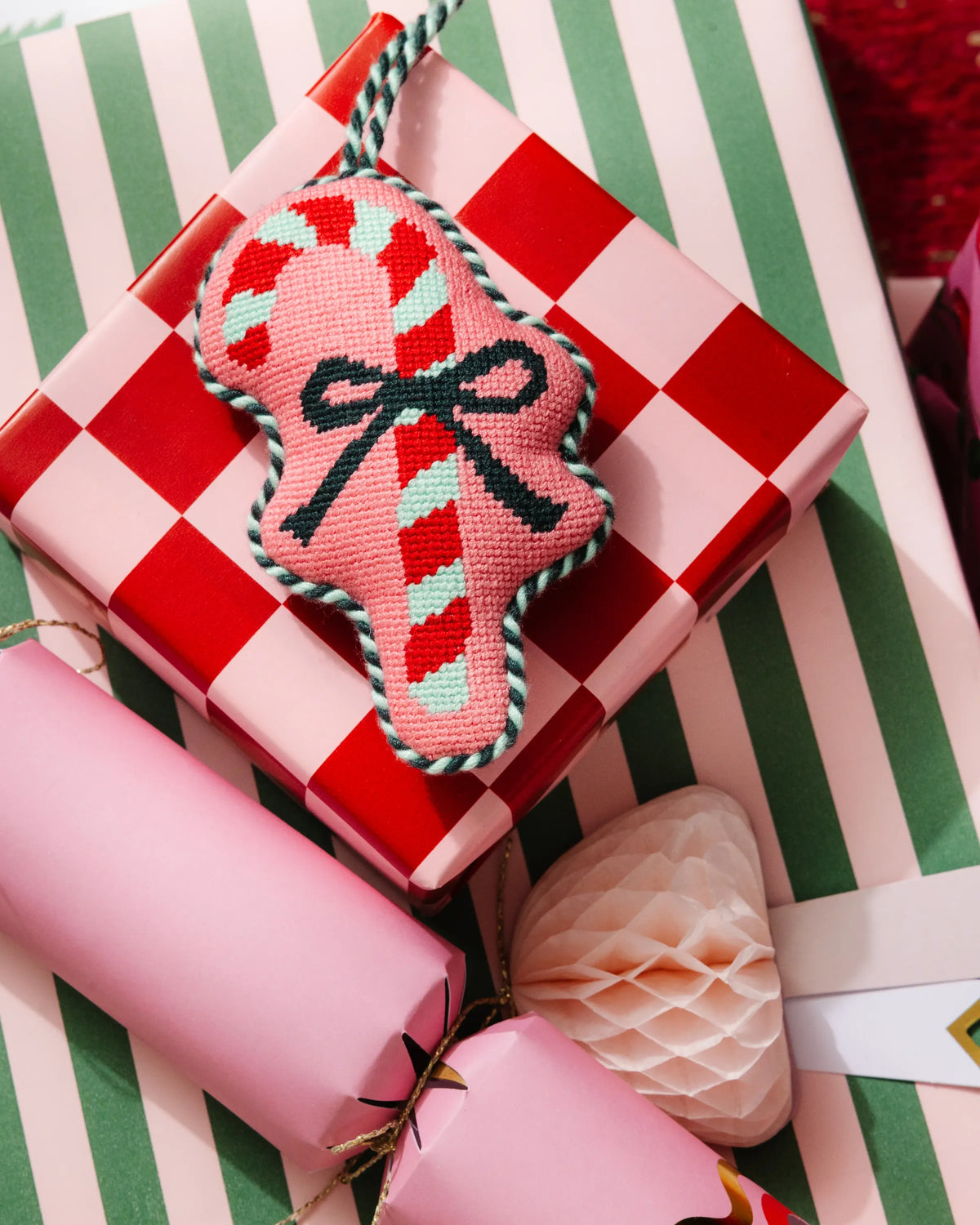 Candy cane needlepoint ornament on red-and-green striped gift wrap