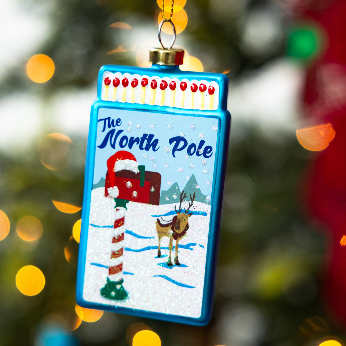 Blue “The North Pole” matchbook ornament with reindeer and snowy winter scene.
