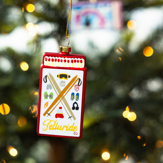 Red Telluride matchbook ornament hanging on a Christmas tree with gold cord