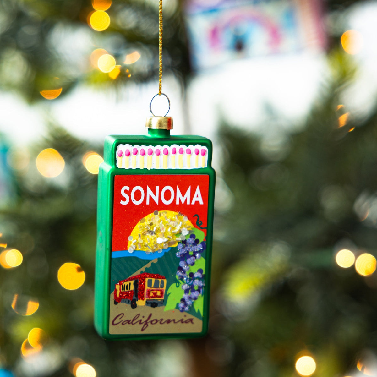 Green matchbook-style Sonoma ornament hanging on a Christmas tree