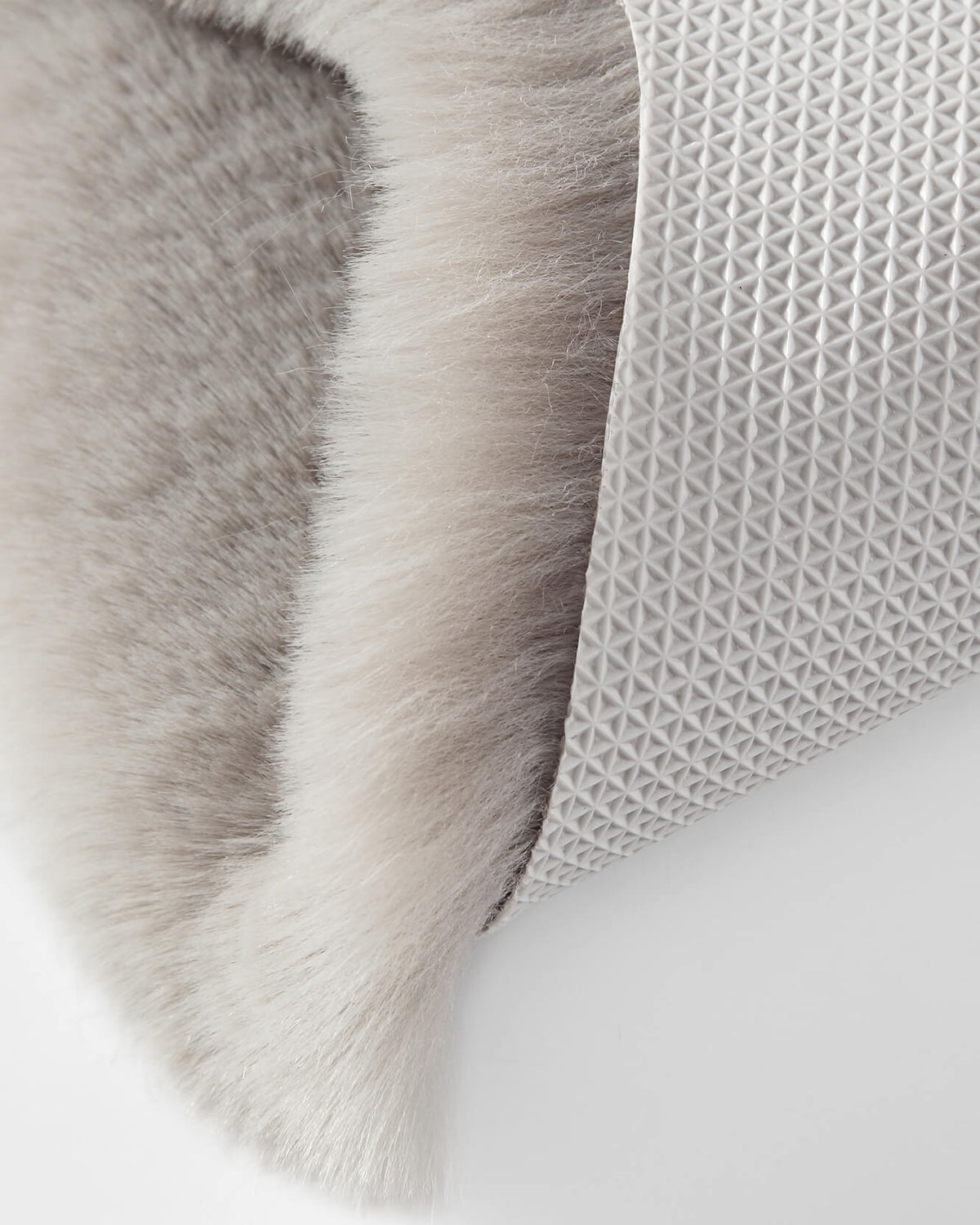 Grey faux fur rug corner with textured backing on a light surface