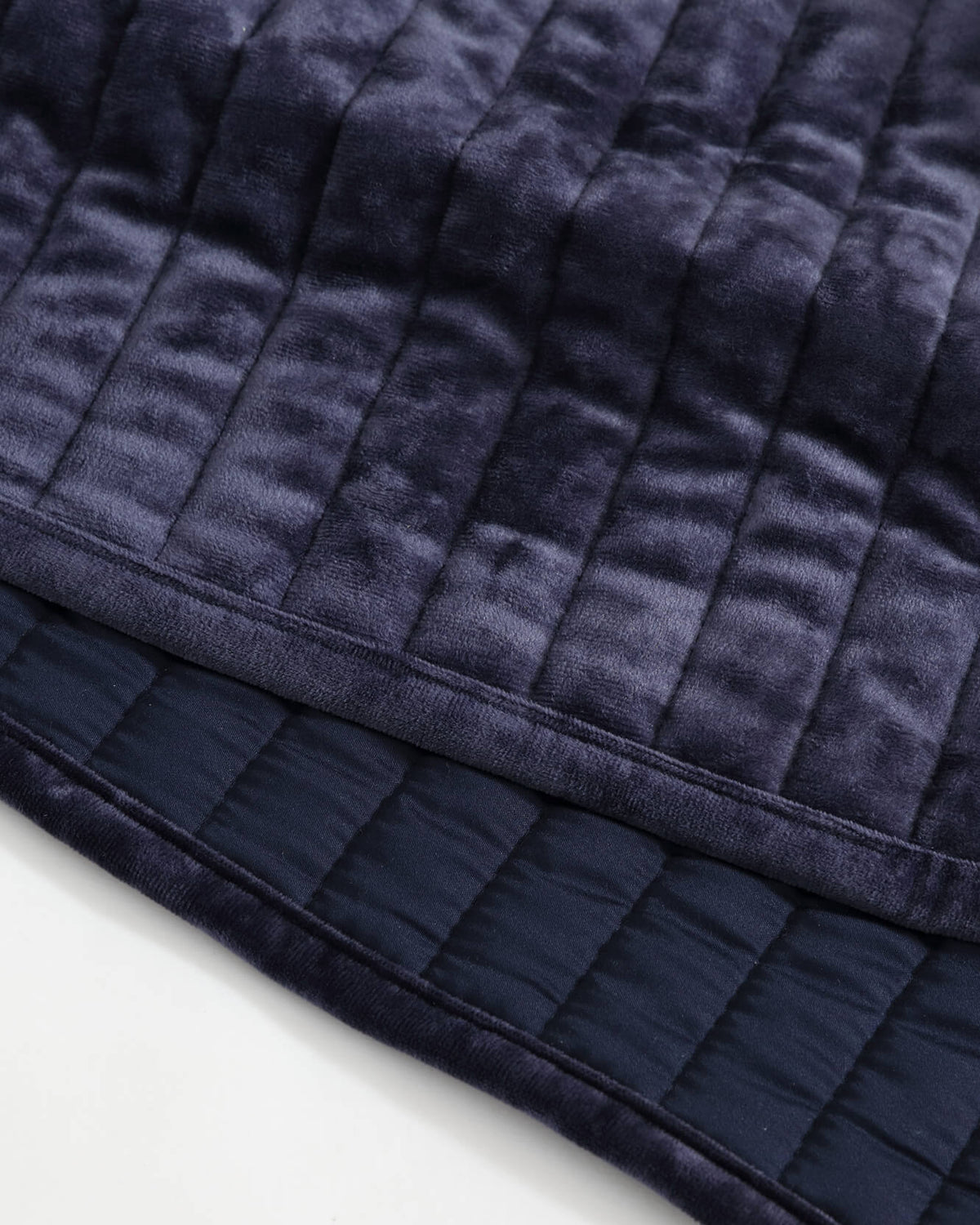 Dark blue velvet quilt close-up with raised channel stripes and stitched border.