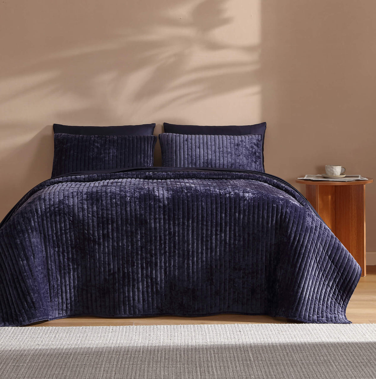 Dark blue velvet quilt on a bed with thick channel stitching texture.