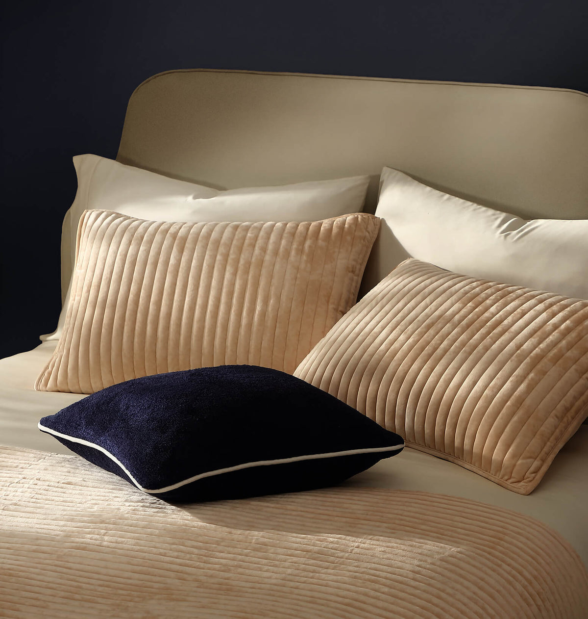 Velvet channel quilt blanket in beige with raised vertical ribs, folded at bed edge
