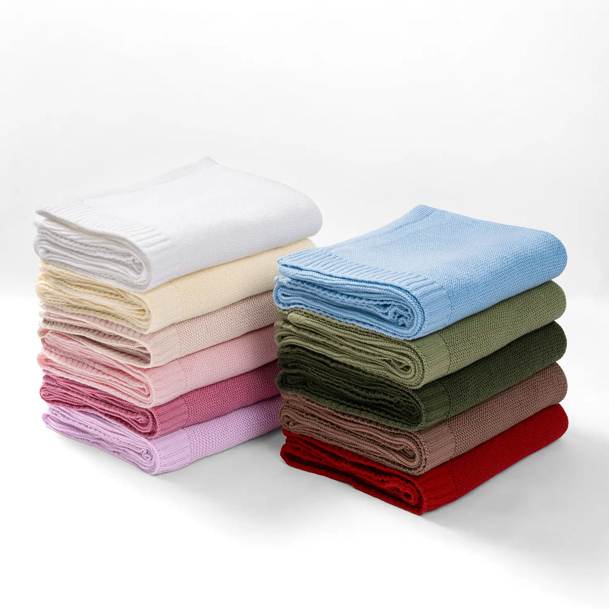 Stack of folded knit baby blankets, including a cream one with ribbed trim.