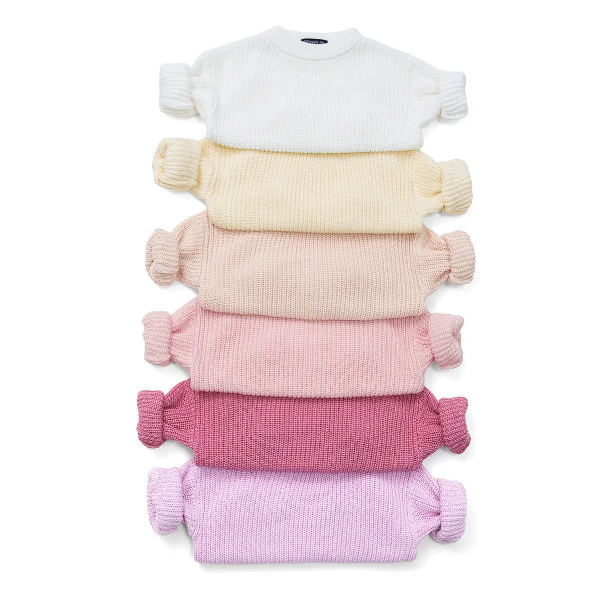 Stack of knit baby sweaters in white, yellow, pink, rose, purple; pom-pom cuffs