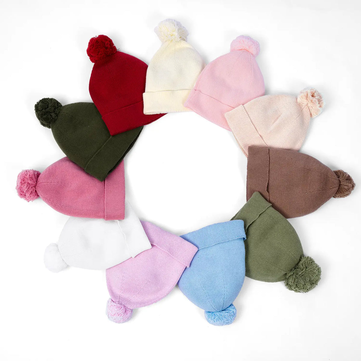 Sage green knit baby beanie with pom-pom, shown among mixed colors.