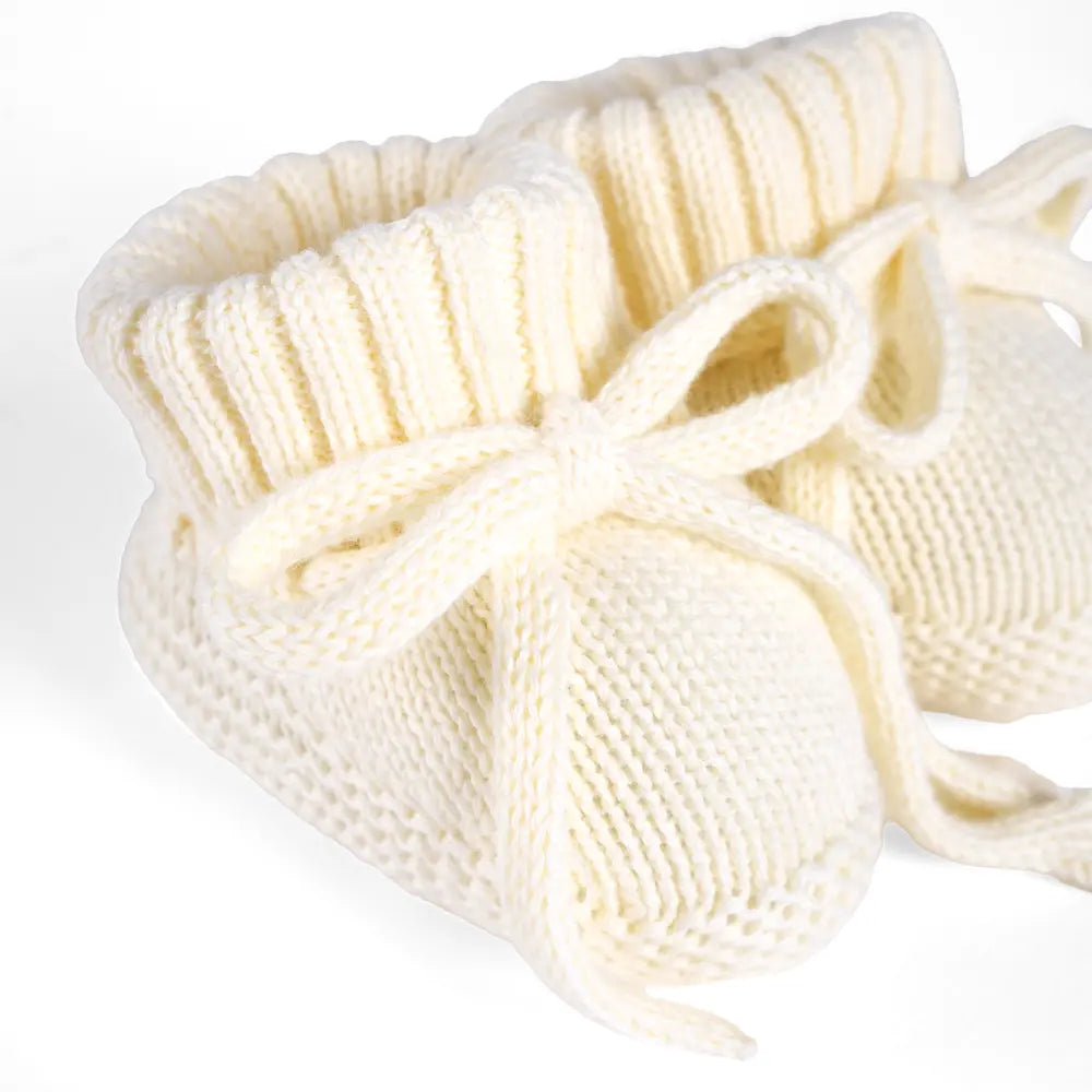 Cream knitted baby booties detail view with ribbed cuffs and bow ties