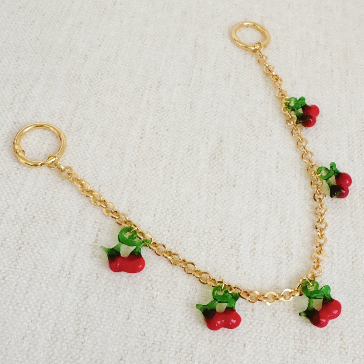 Gold chain bag charm featuring red cherry drop charms with green leaves