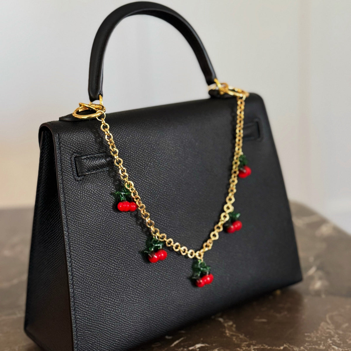 Gold chain bag charm with red cherry drops hanging from black bag handle