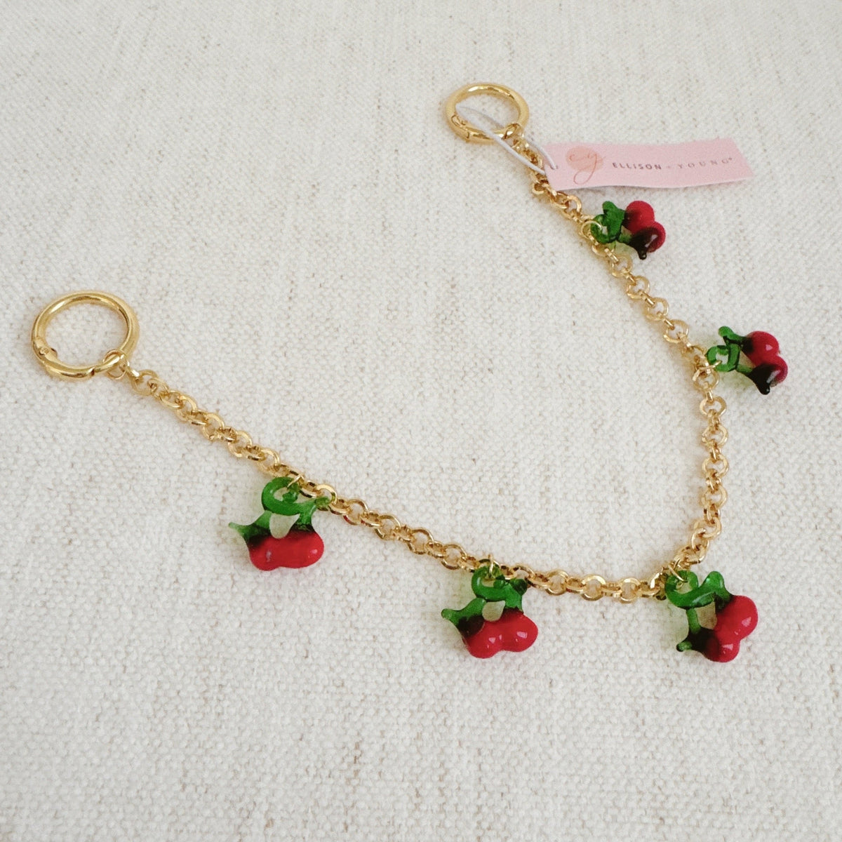 Gold chain bag charm with red cherry drops, green leaves, and pink tag