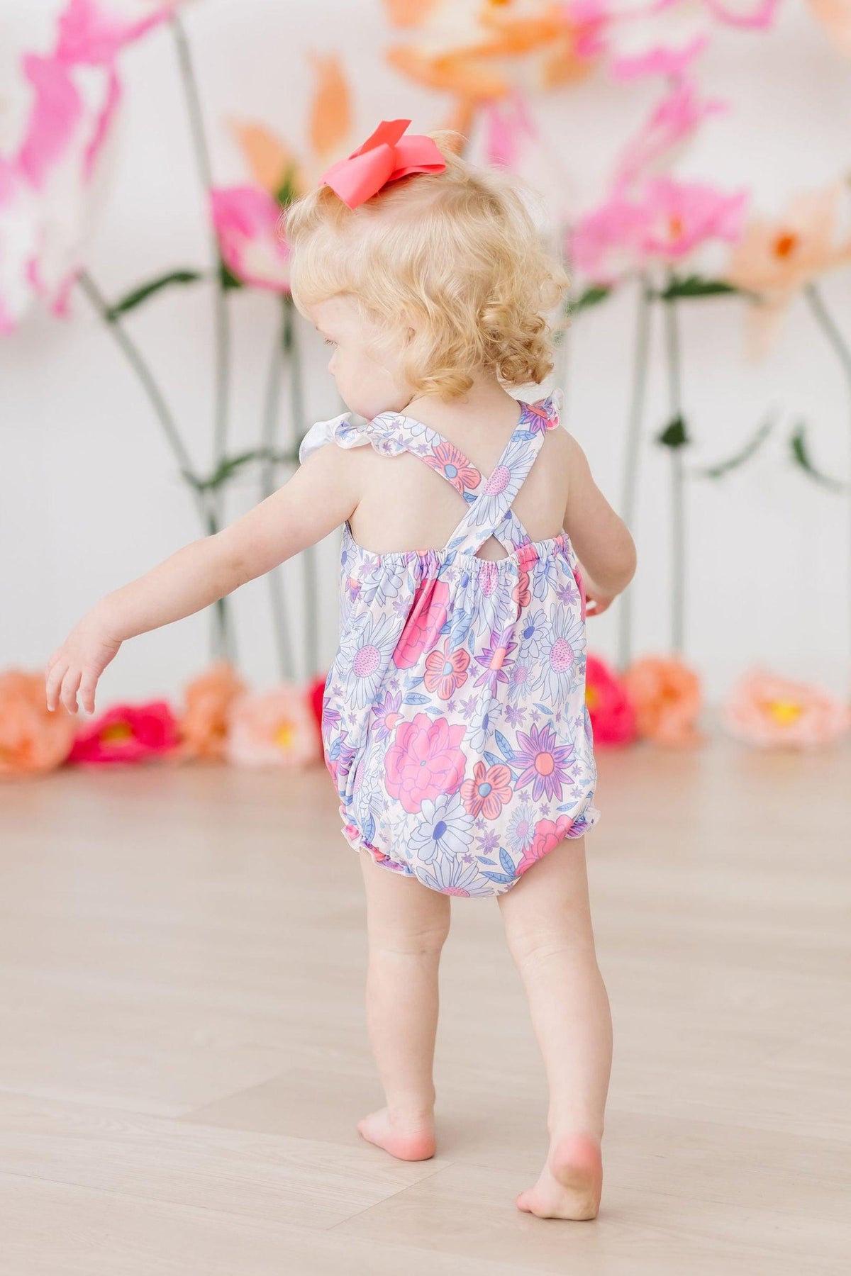 Pastel floral ruffle cross-back romper with crisscross straps visible from behind