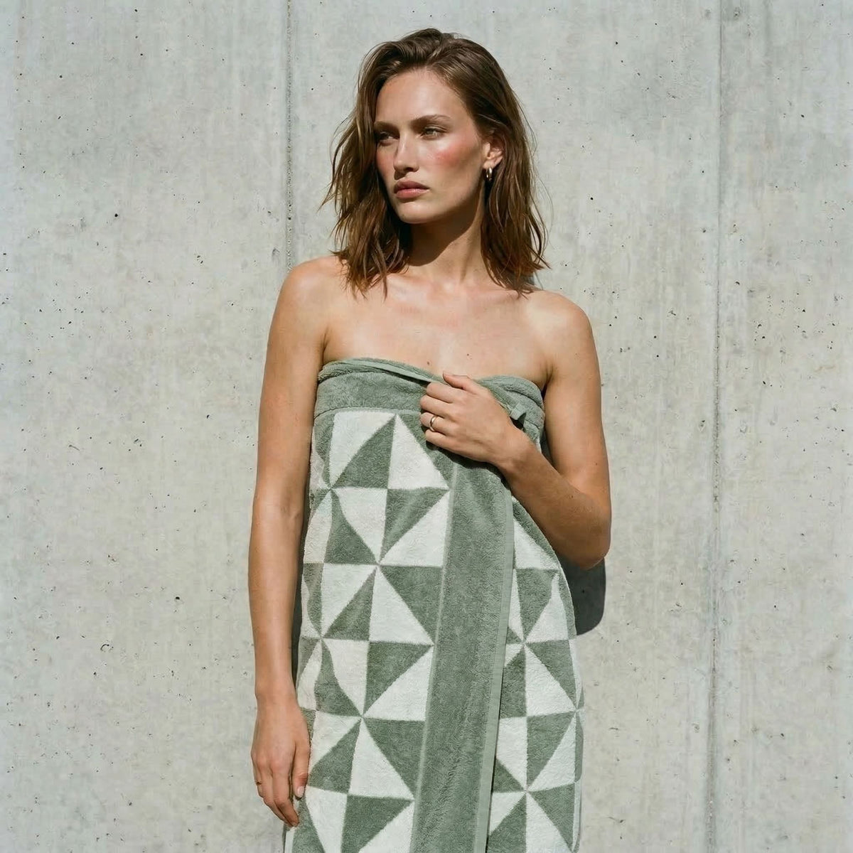 Sage and ecru geometric cotton towel with triangle pattern, draped over a person’s shoulder.