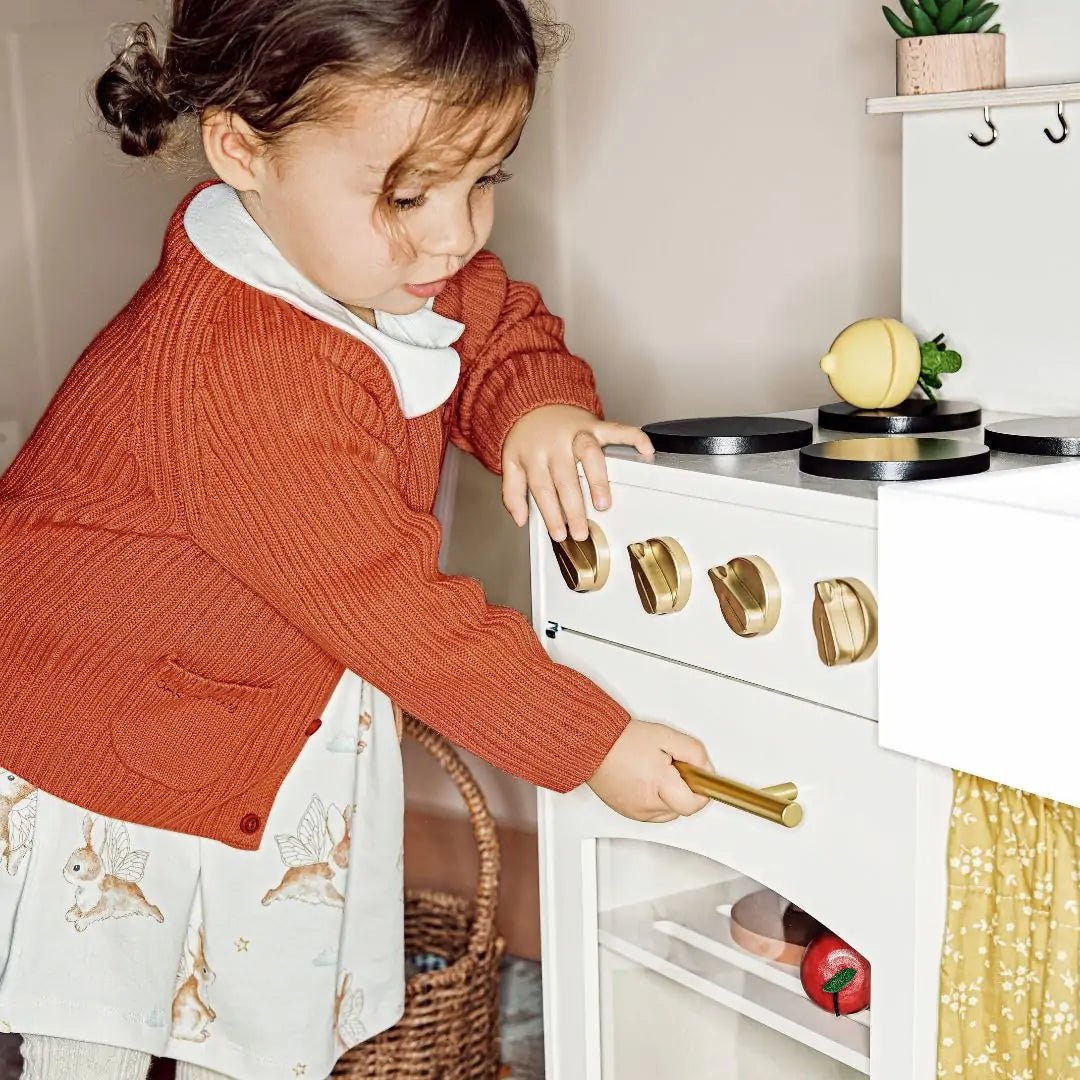 Wooden play kitchen with white oven, black burners and gold knobs