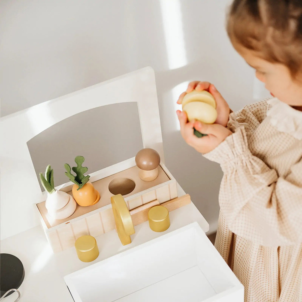 Wooden play kitchen sink with gold faucet and colorful toy produce
