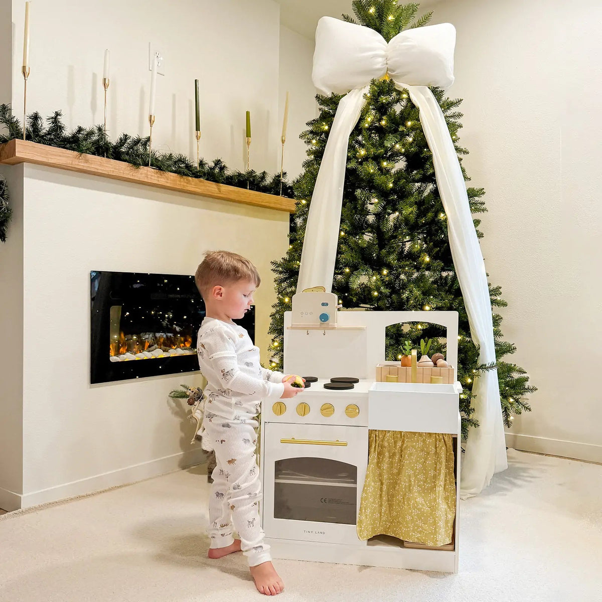 Wooden play kitchen with white oven, sink, gold knobs and fabric curtain
