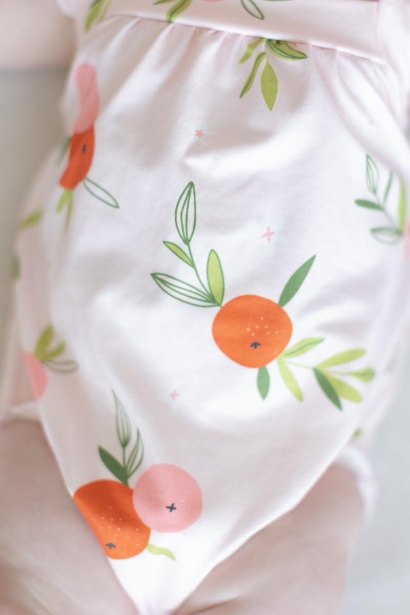 Close-up of light pink romper fabric with orange and leaf fruit pattern