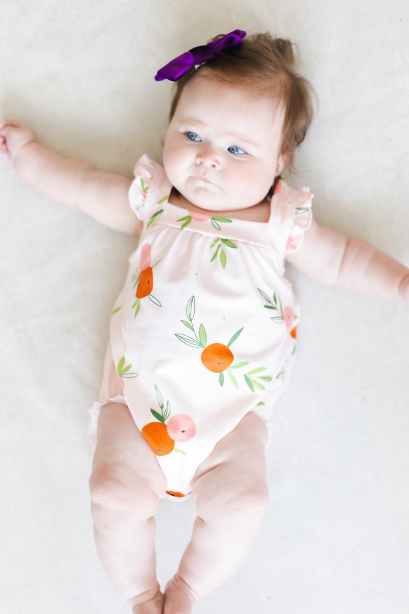 Baby in light pink fruit-print ruffle romper with orange motif