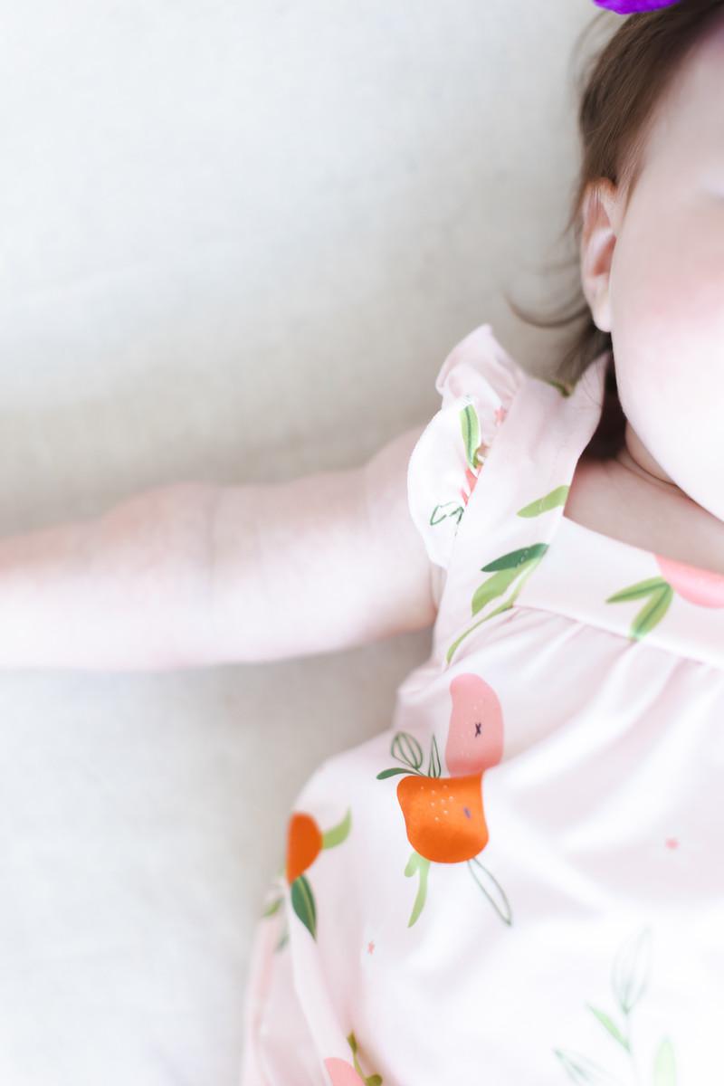 Side view of baby in light pink fruit-print romper with ruffle shoulder detail