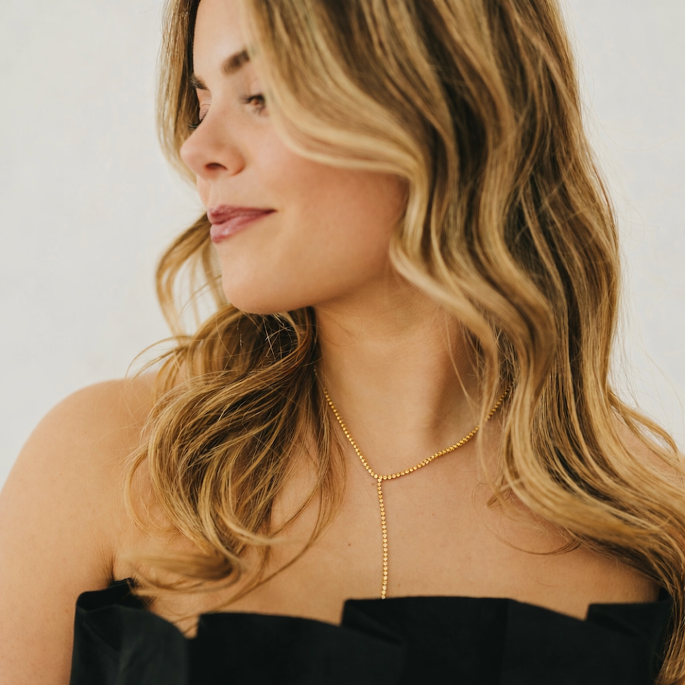Gold tennis lariat necklace on a woman, with a vertical drop pendant