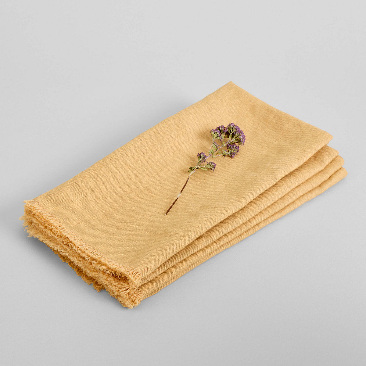 Mustard linen napkin with small purple flowers, folded with fringed edge