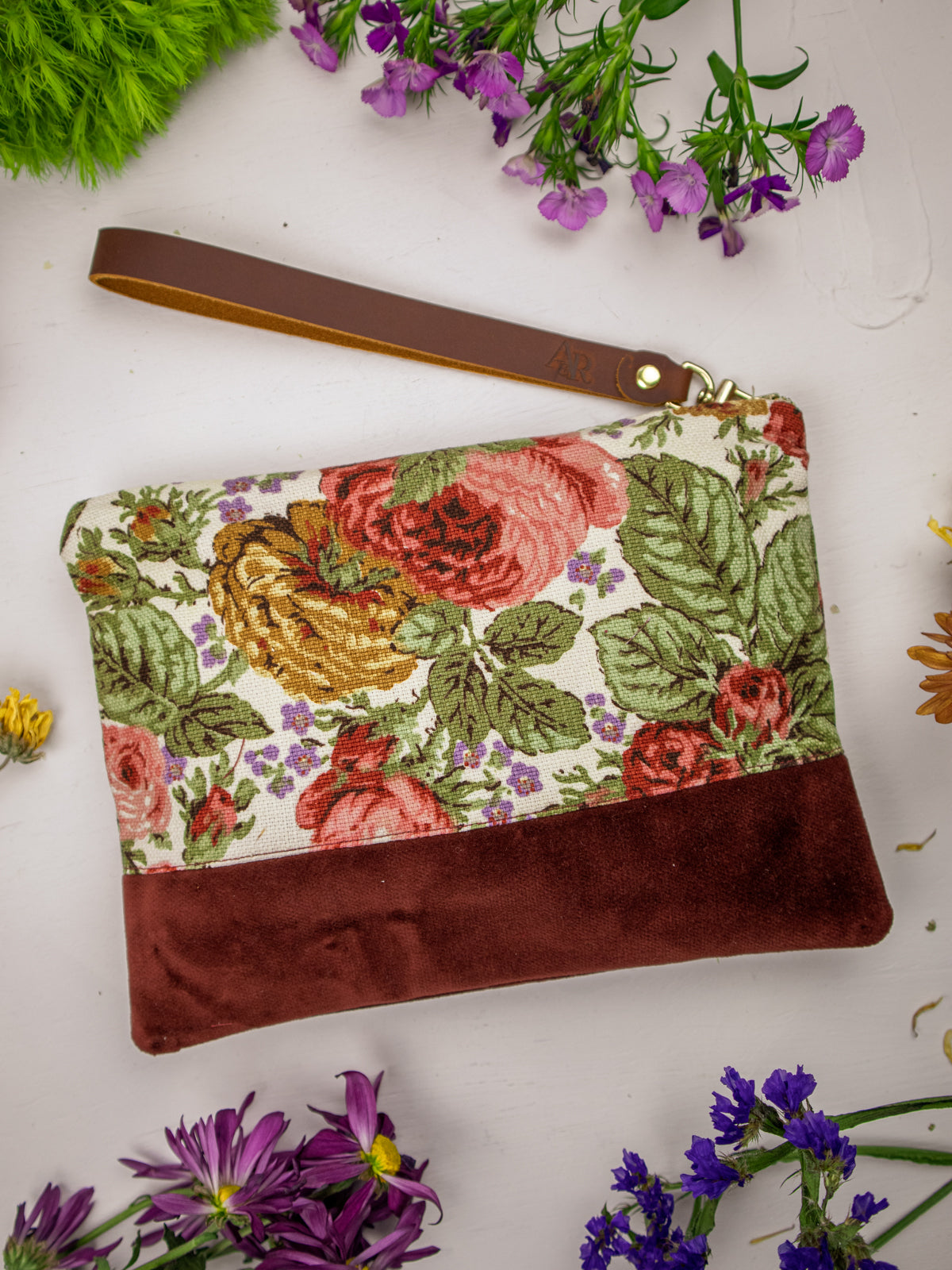 Wristlet purse with floral fabric top, brown suede bottom, and wrist strap with gold ring.