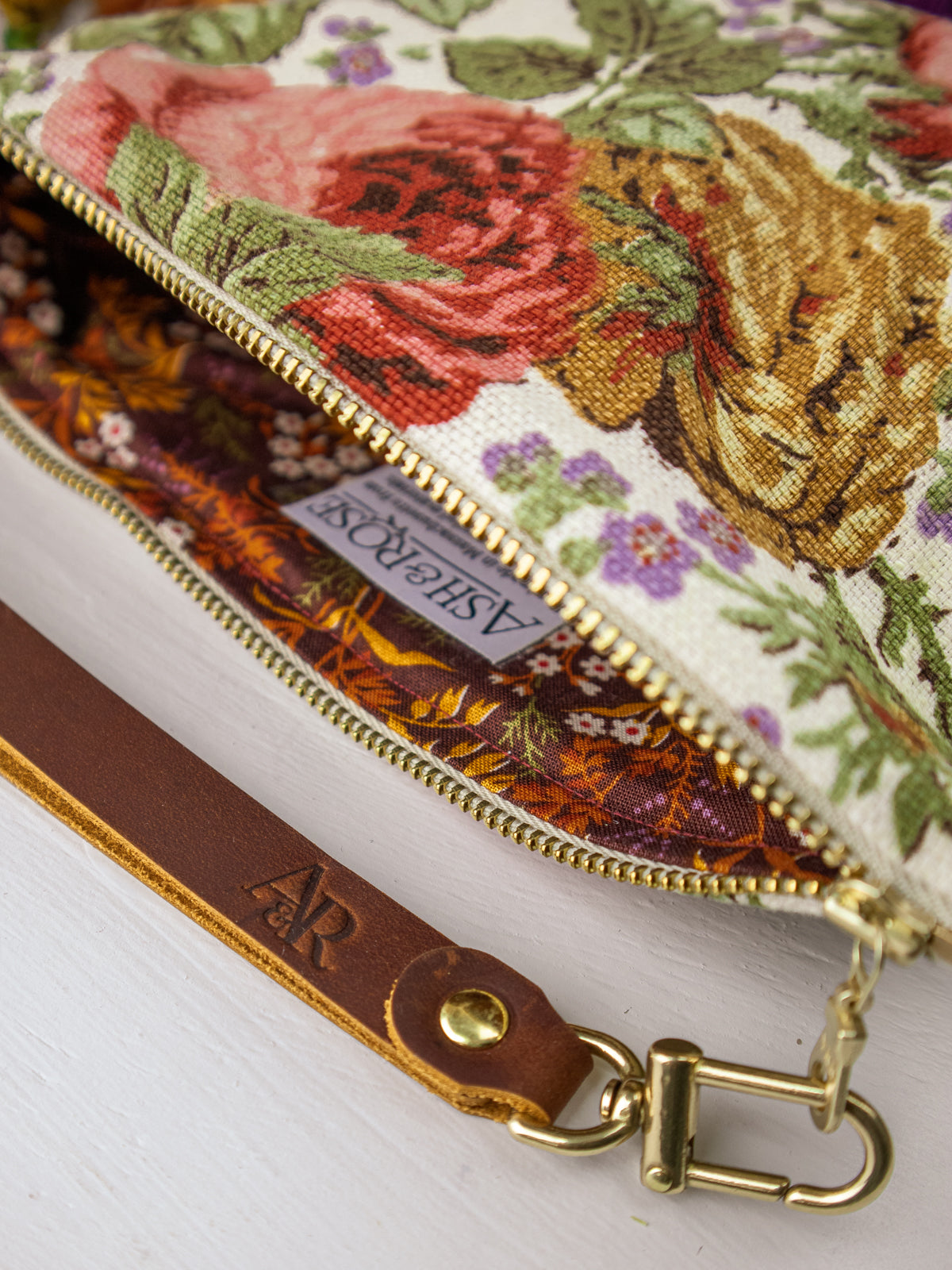 Wristlet purse close-up: gold zipper, floral lining, and brown leather trim with logo tag.