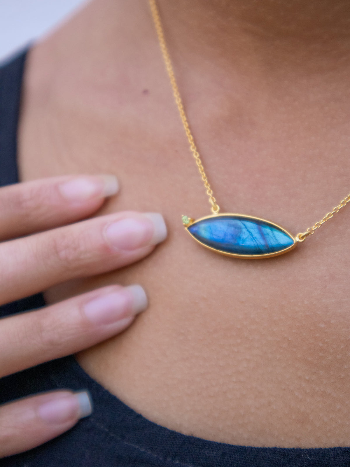 Close-up of gold chain necklace with oval blue gemstone pendant