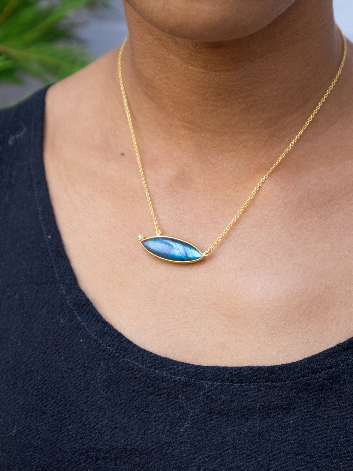 Gold chain necklace with oval blue gemstone pendant on neckline