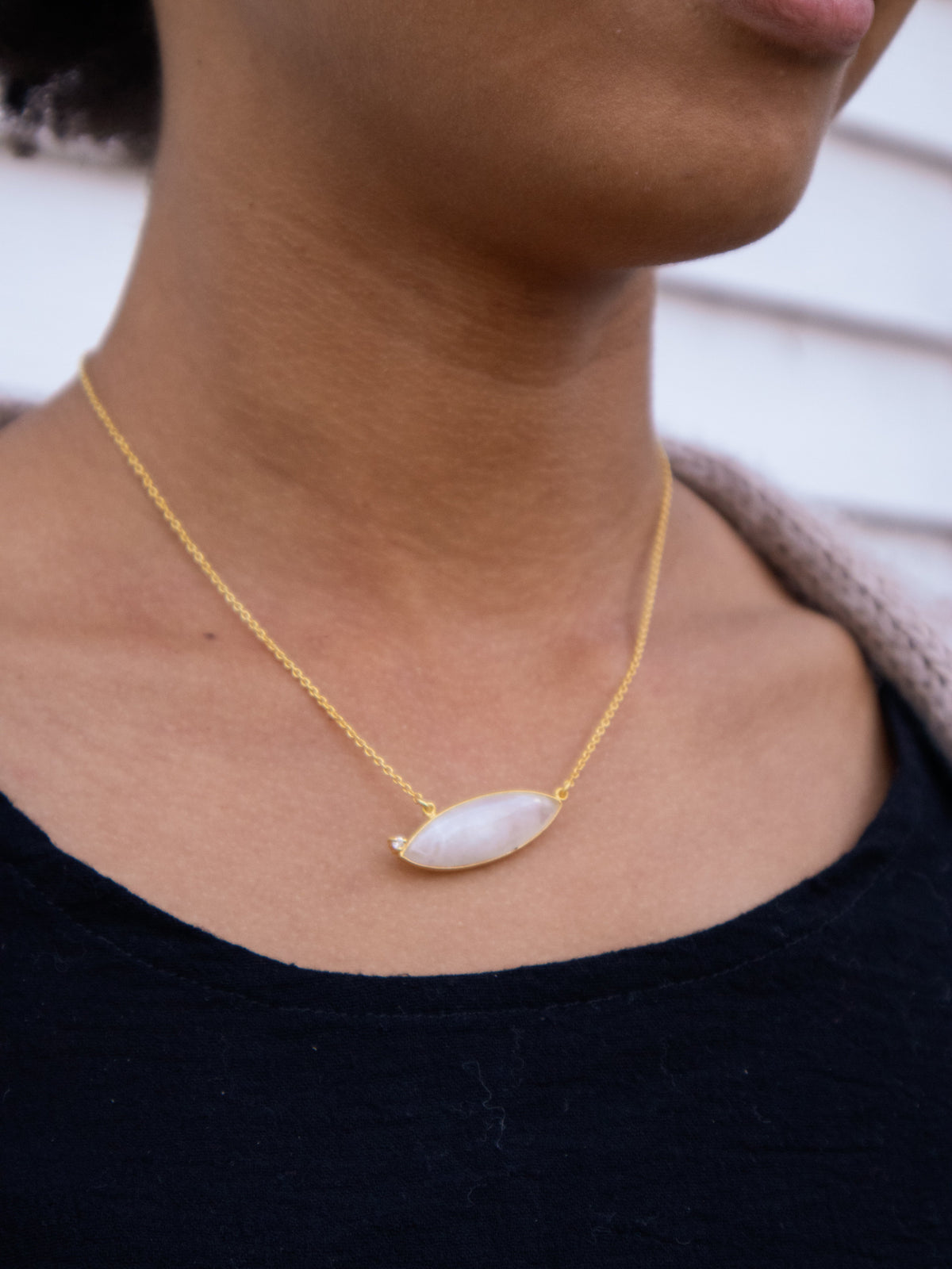 Gold chain necklace with oval white gemstone pendant at the throat