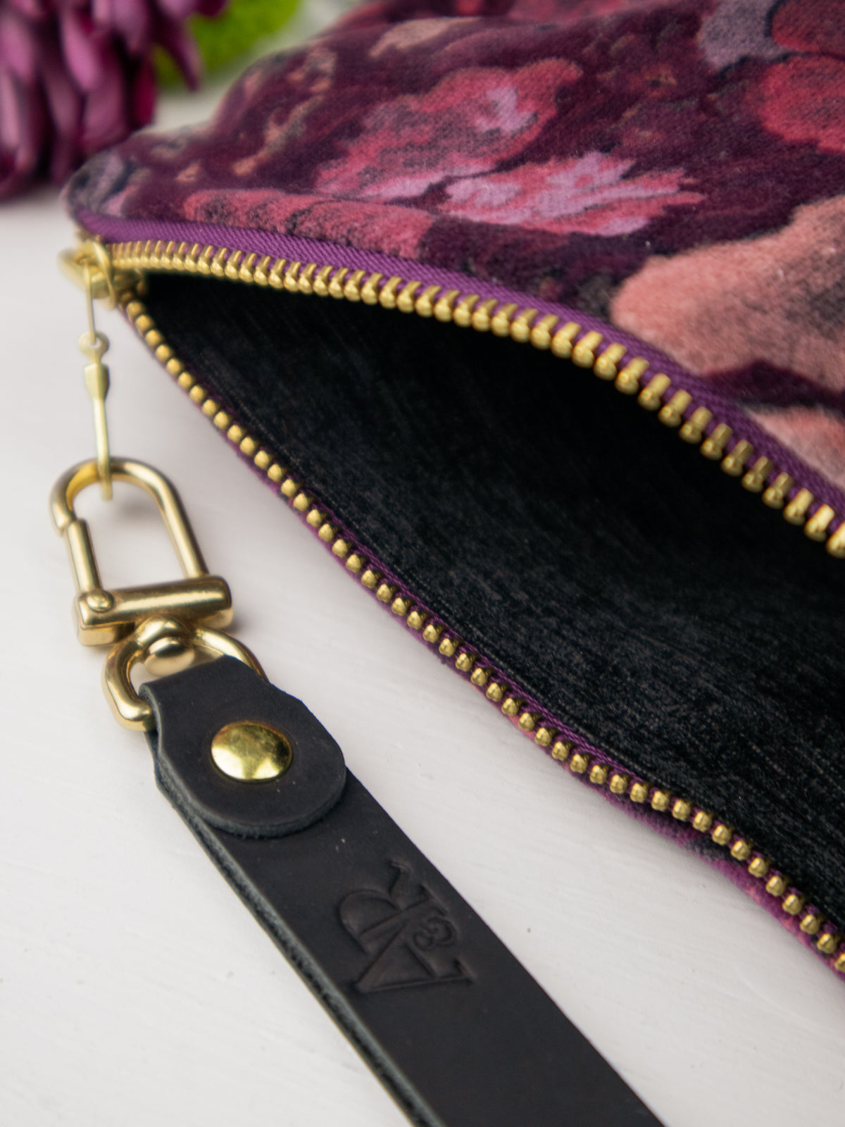 Velvet wristlet close-up: gold zipper teeth, black strap, snap clasp hardware.