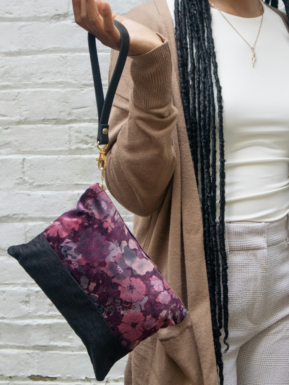 Velvet wristlet hanging from gold strap, purple floral panel with black bottom.