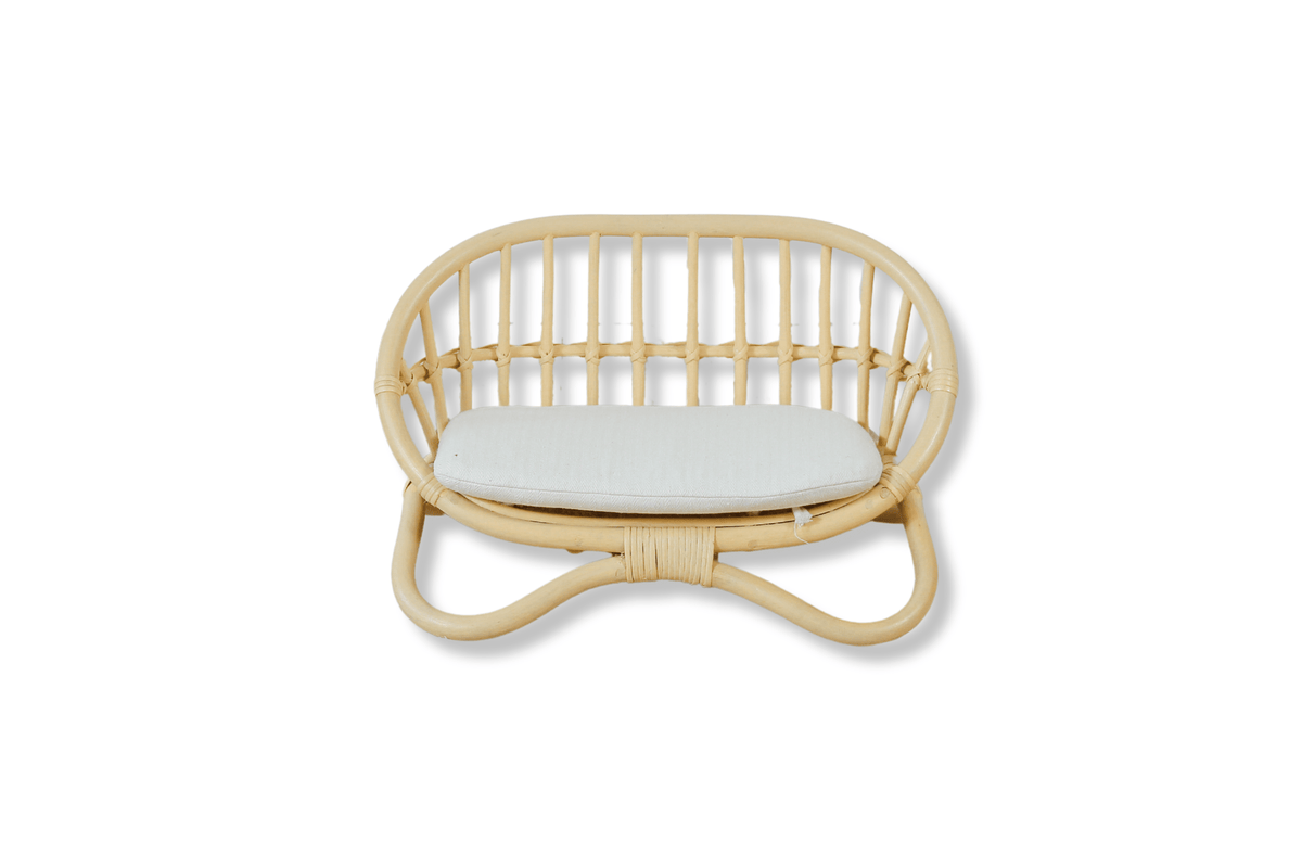 Natural rattan miniature doll couch with curved slatted back and white seat cushion