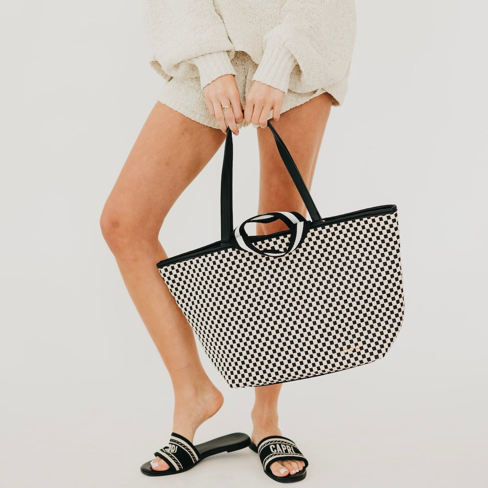 Checkered woven tote bag with black top handles and striped trim