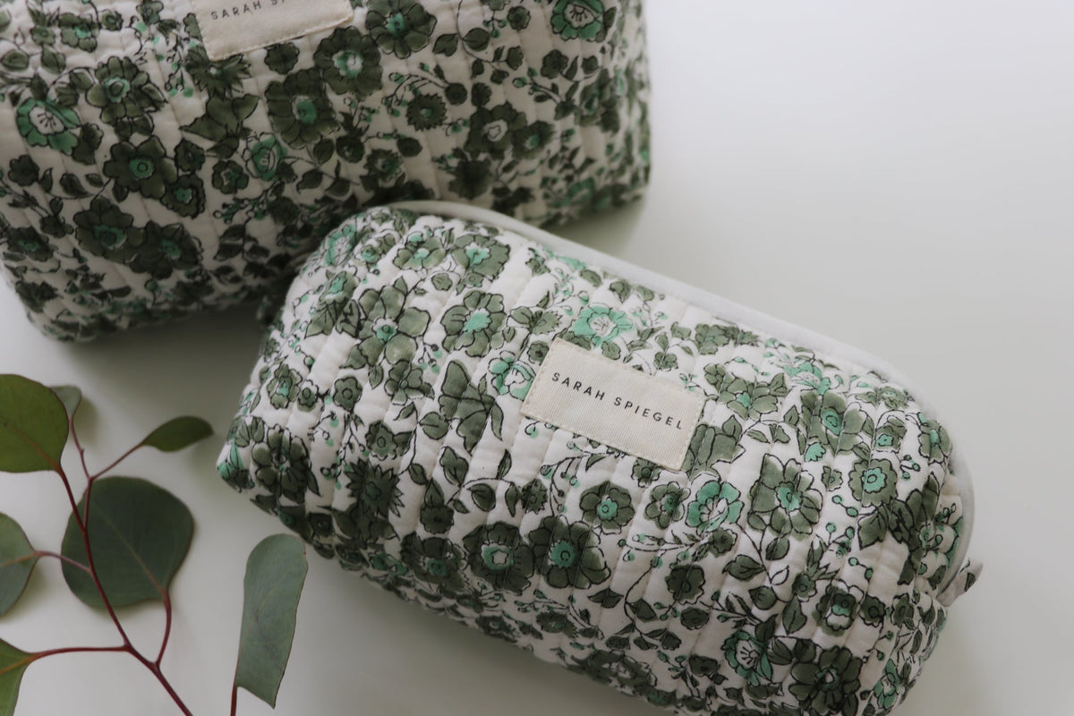 Quilted floral toiletry pouch with a zip closure and brand label, shown beside the matching bag.