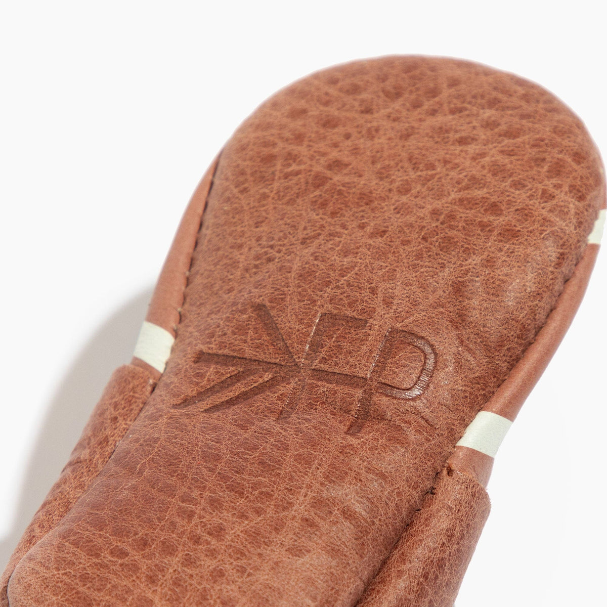 Brown baby shoe upper with stitched H logo detail and white stripe, close-up