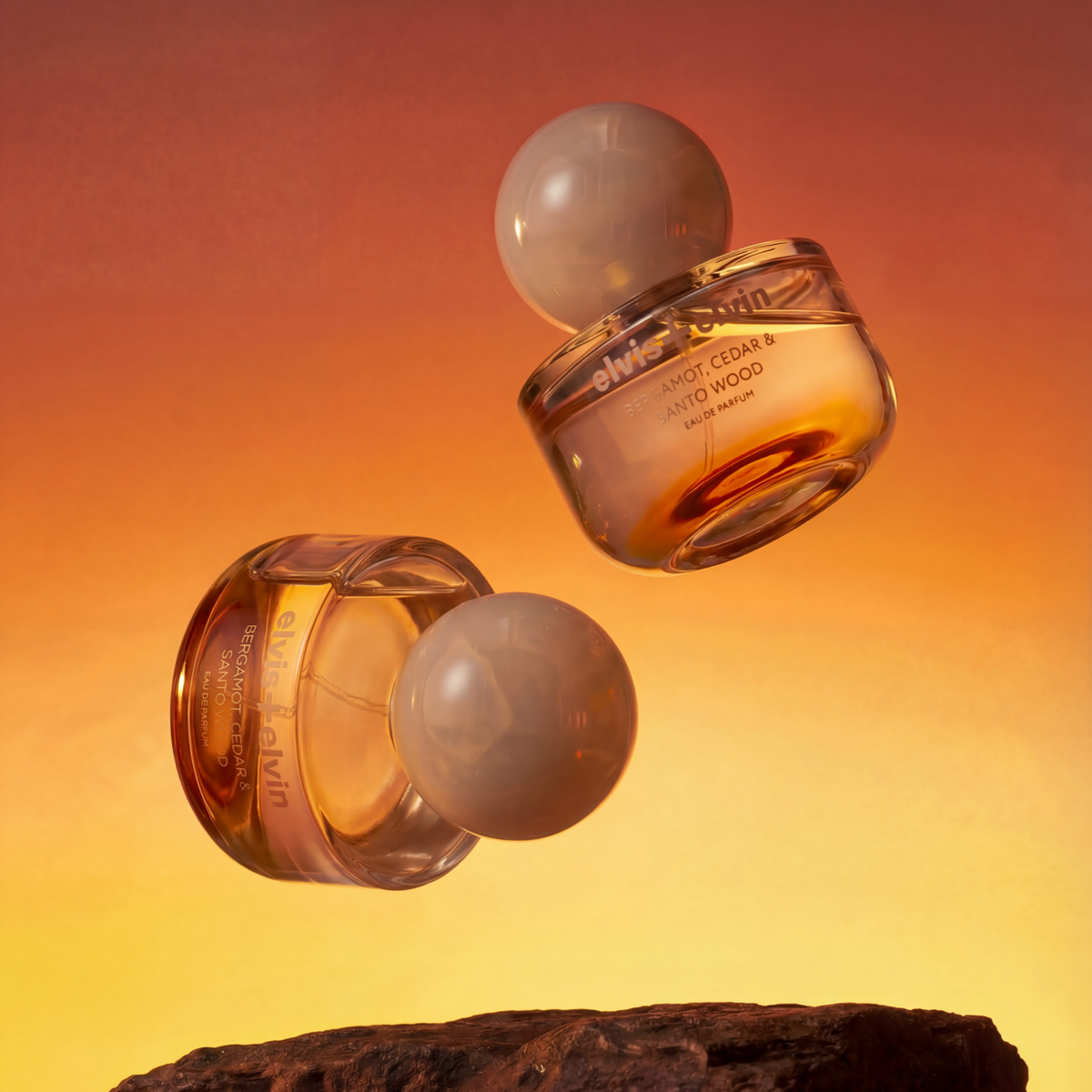 Two glass eau de parfum bottles with amber liquid and clear globe caps