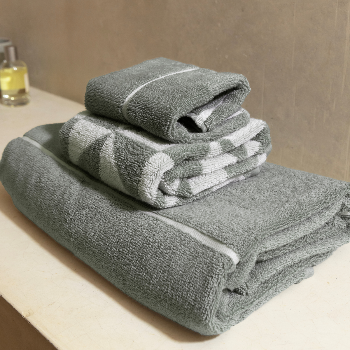 Sage-green cotton towels with white stripe accents, folded and stacked