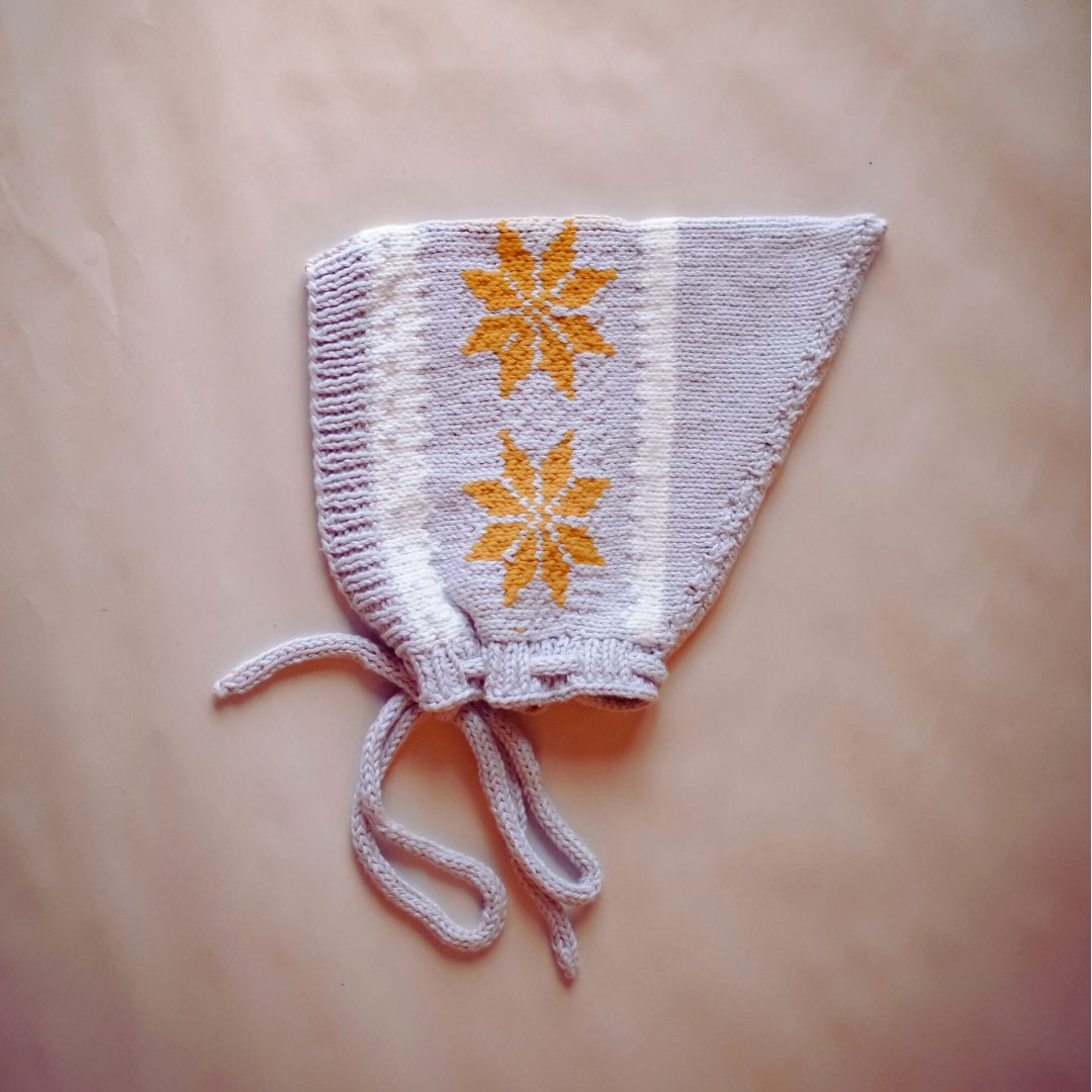 Knit pixie hat in light gray with orange star motifs and tied ear strings