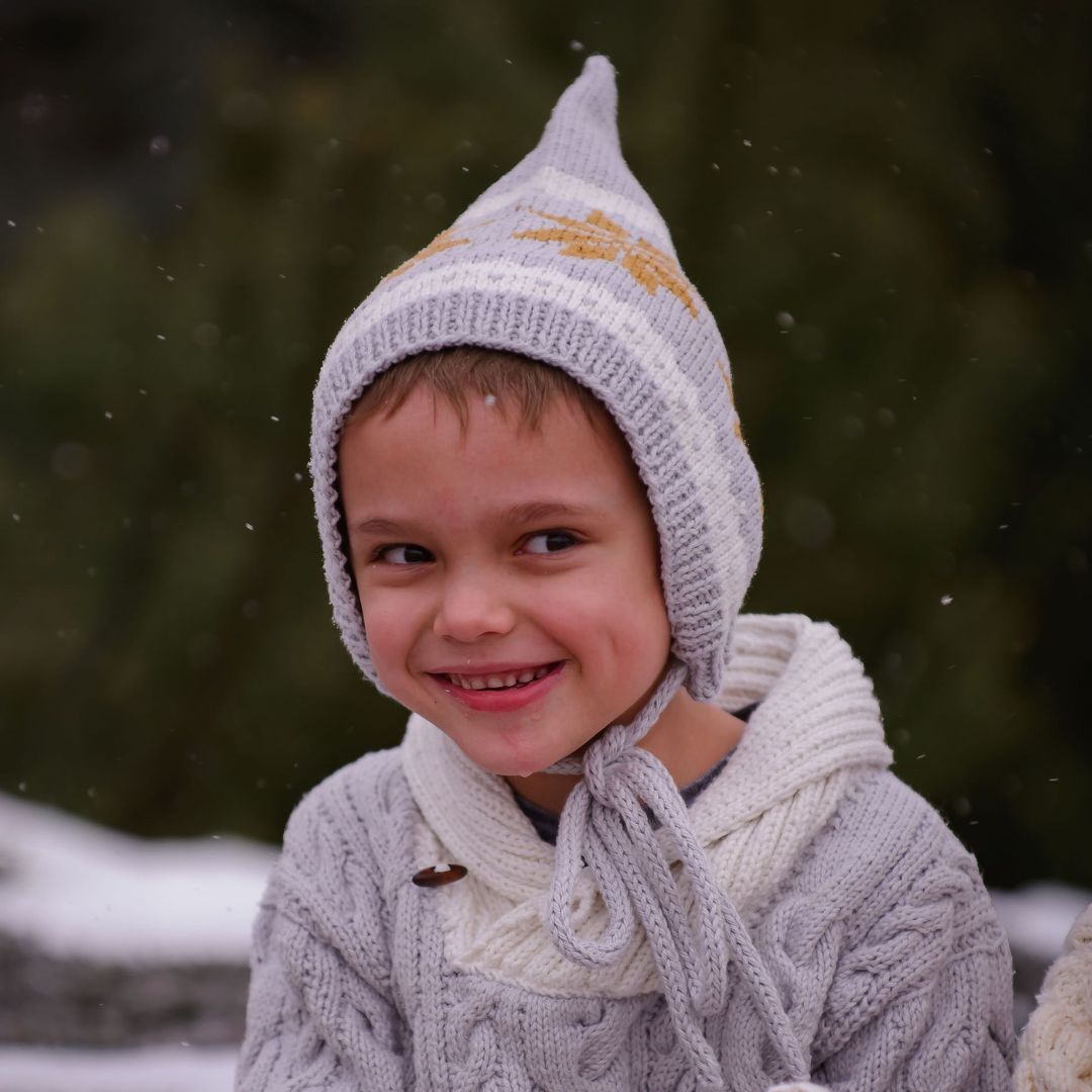 Light gray knit pixie hat with mustard star pattern and dangling ear ties